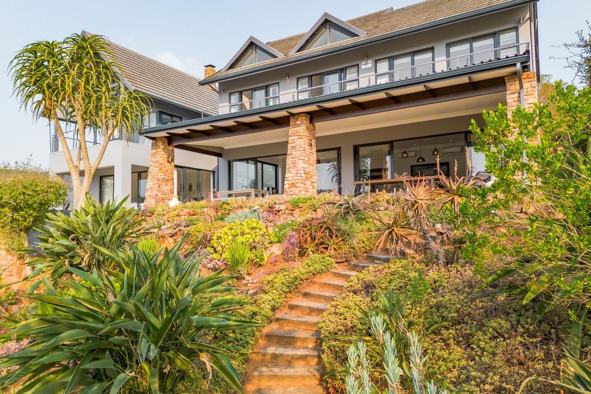 A beautiful multi-level residence featuring a stone-clad patio, landscaped terraced garden with stone steps, and modern architectural design with large glass sliding doors.
