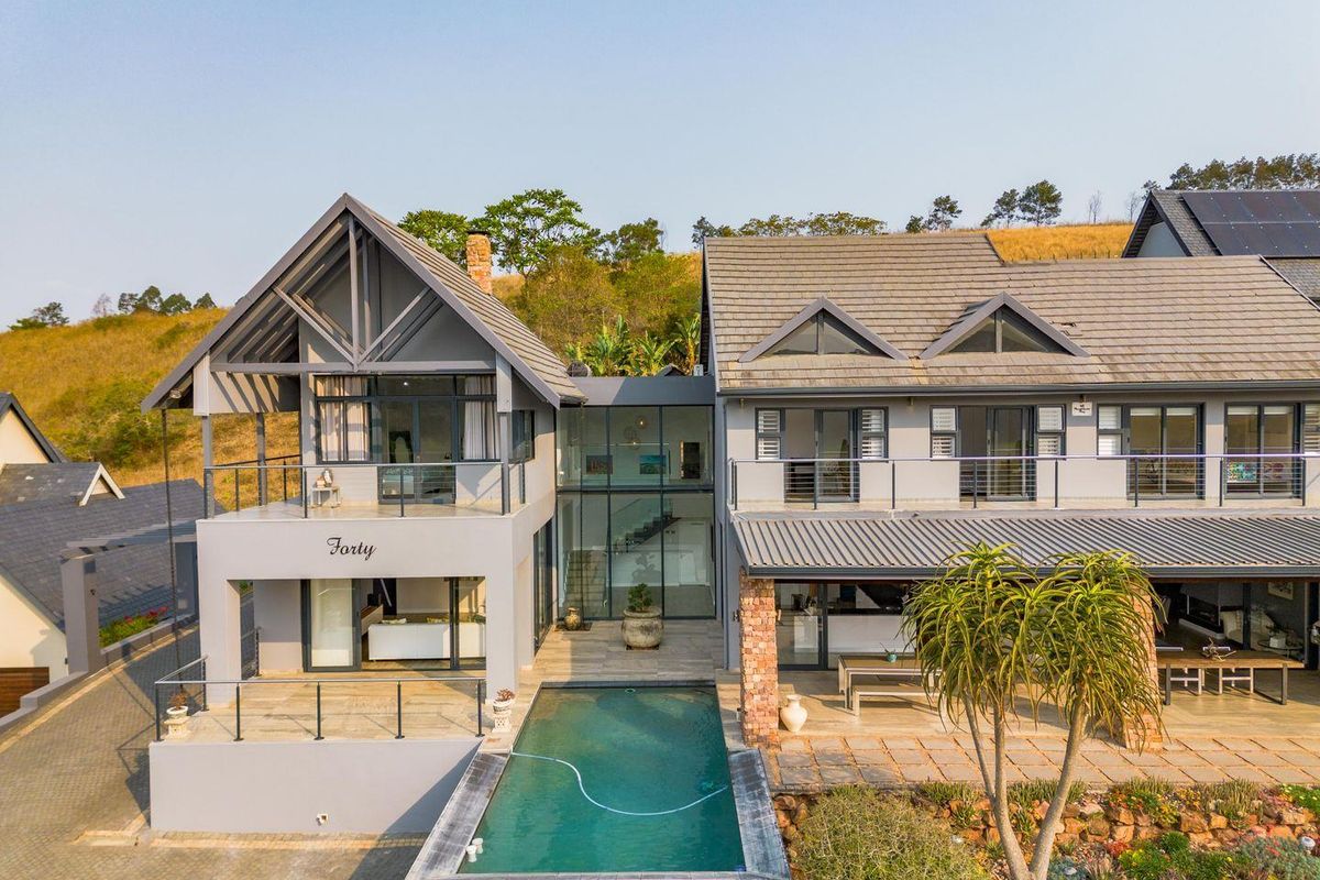 Aerial view of a modern multi-level residence featuring a swimming pool, expansive glass facade, covered patio, and contemporary architectural design.