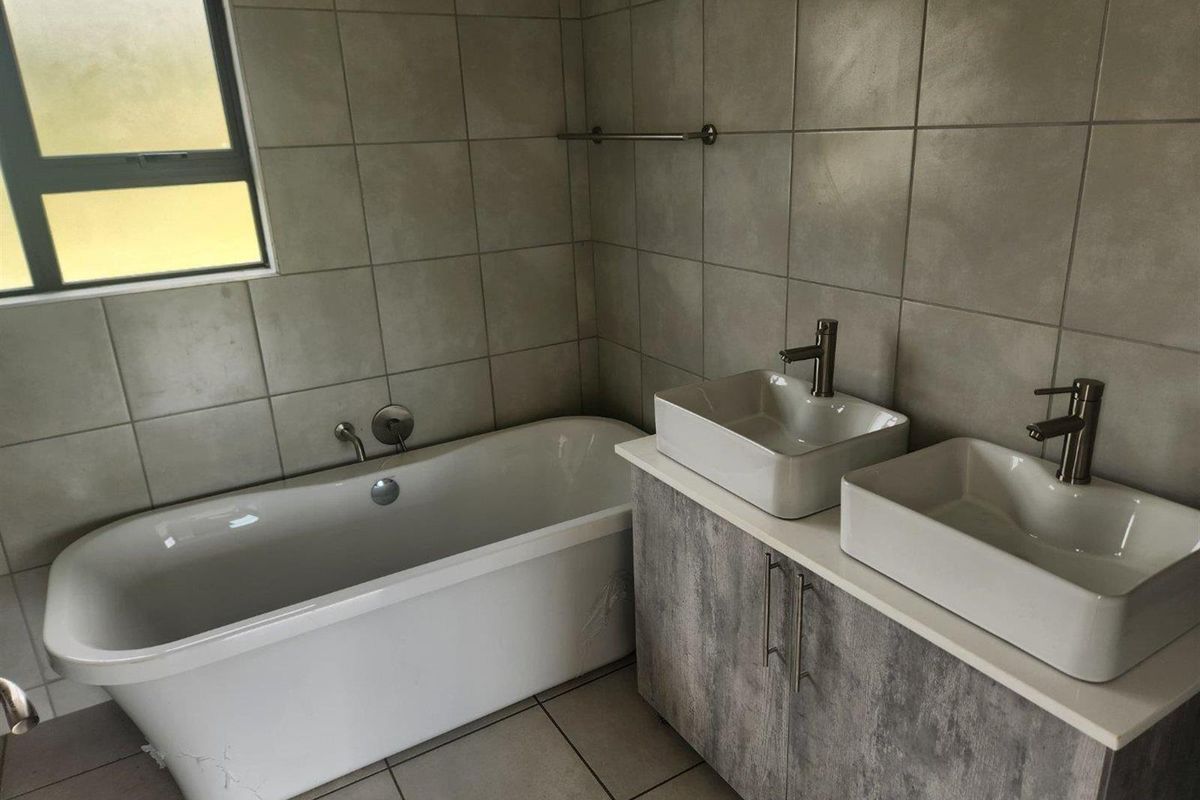 Modern bathroom featuring a freestanding bathtub, double vessel sinks with contemporary faucets, and neutral wall tiling.