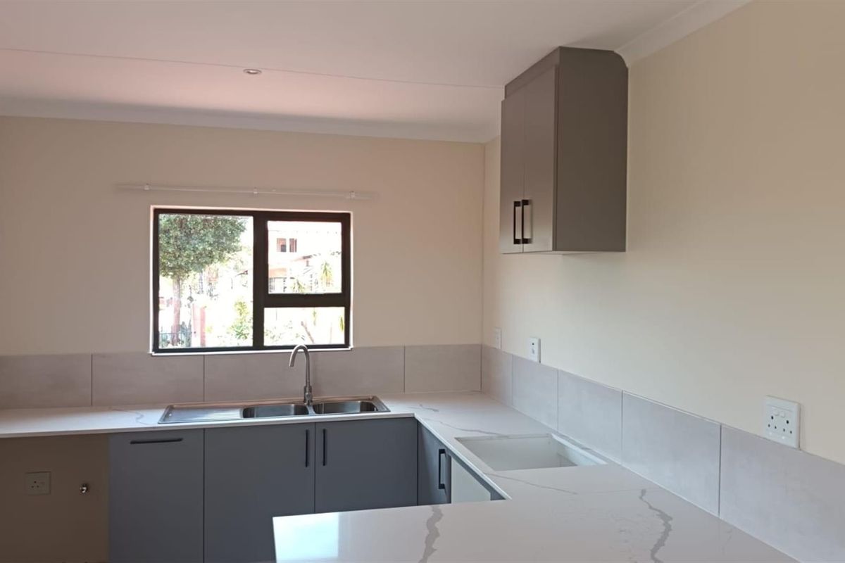 Modern kitchen featuring grey cabinetry, stone-look countertops, a stainless steel sink, and tiled splashbacks in a clean, neutral space.