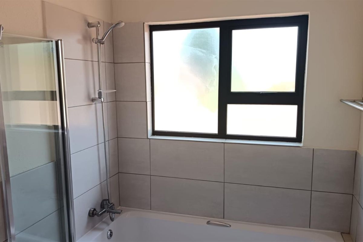 A clean bathroom featuring a bathtub with a wall-mounted shower head, tiled splashbacks, and a modern black-framed window.