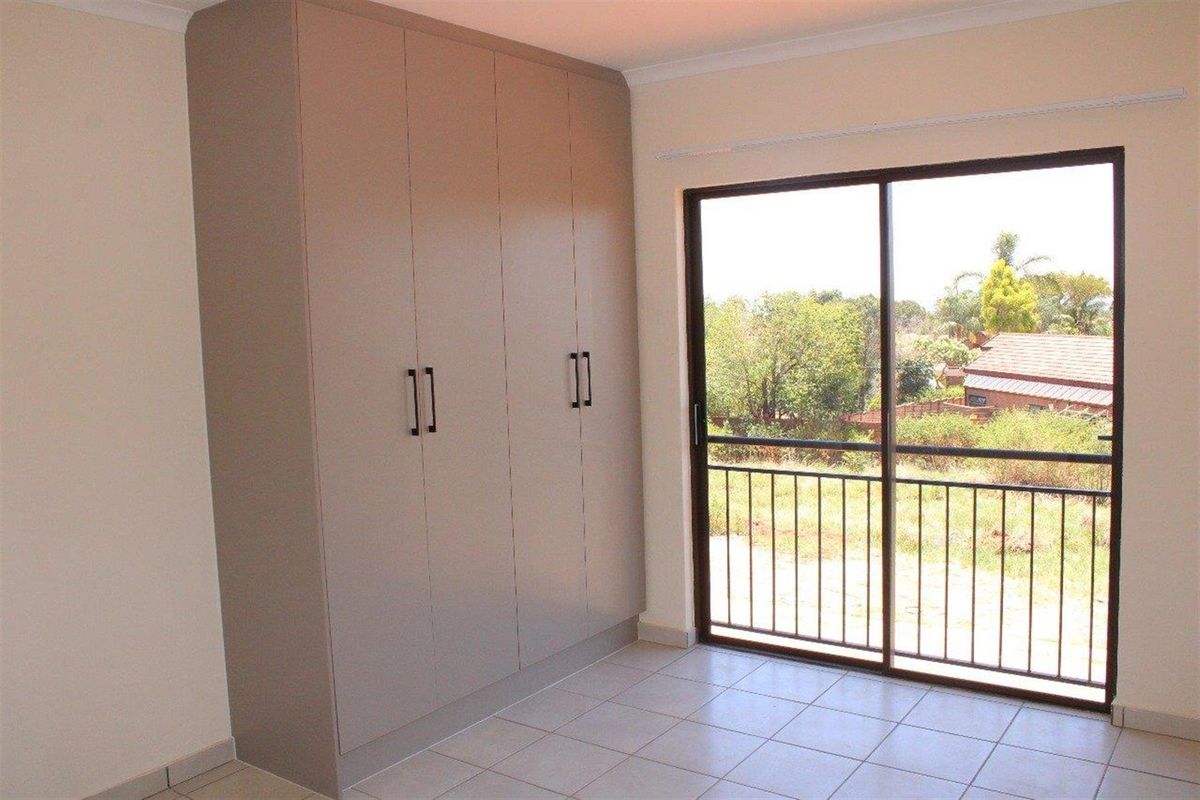 A bright bedroom featuring built-in cupboards, tiled flooring, and a sliding glass door leading to a balcony with outdoor views.