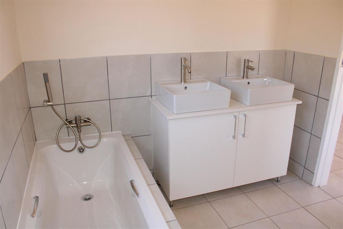 A modern bathroom featuring a double vanity with square vessel sinks and a built-in bathtub with a handheld shower fixture.
