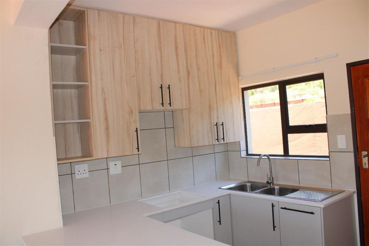 A modern kitchen featuring light wood-grain cabinetry, neutral tiled splashbacks, a double stainless steel sink, and ample counter space.