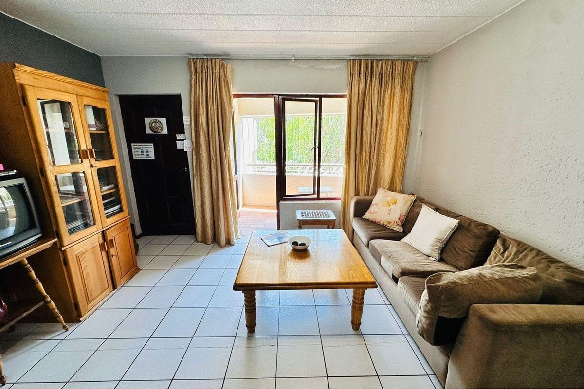 A living room featuring tiled flooring and direct access to a balcony through a glass door, providing natural light to the space.