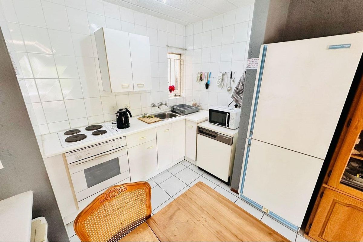 A compact kitchen featuring white cabinetry, tiled walls, a built-in oven with electric hob, and a stainless steel sink.