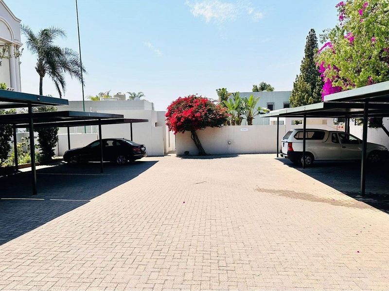 A paved outdoor parking area featuring covered carports for residents, surrounded by perimeter walls and established landscaping.