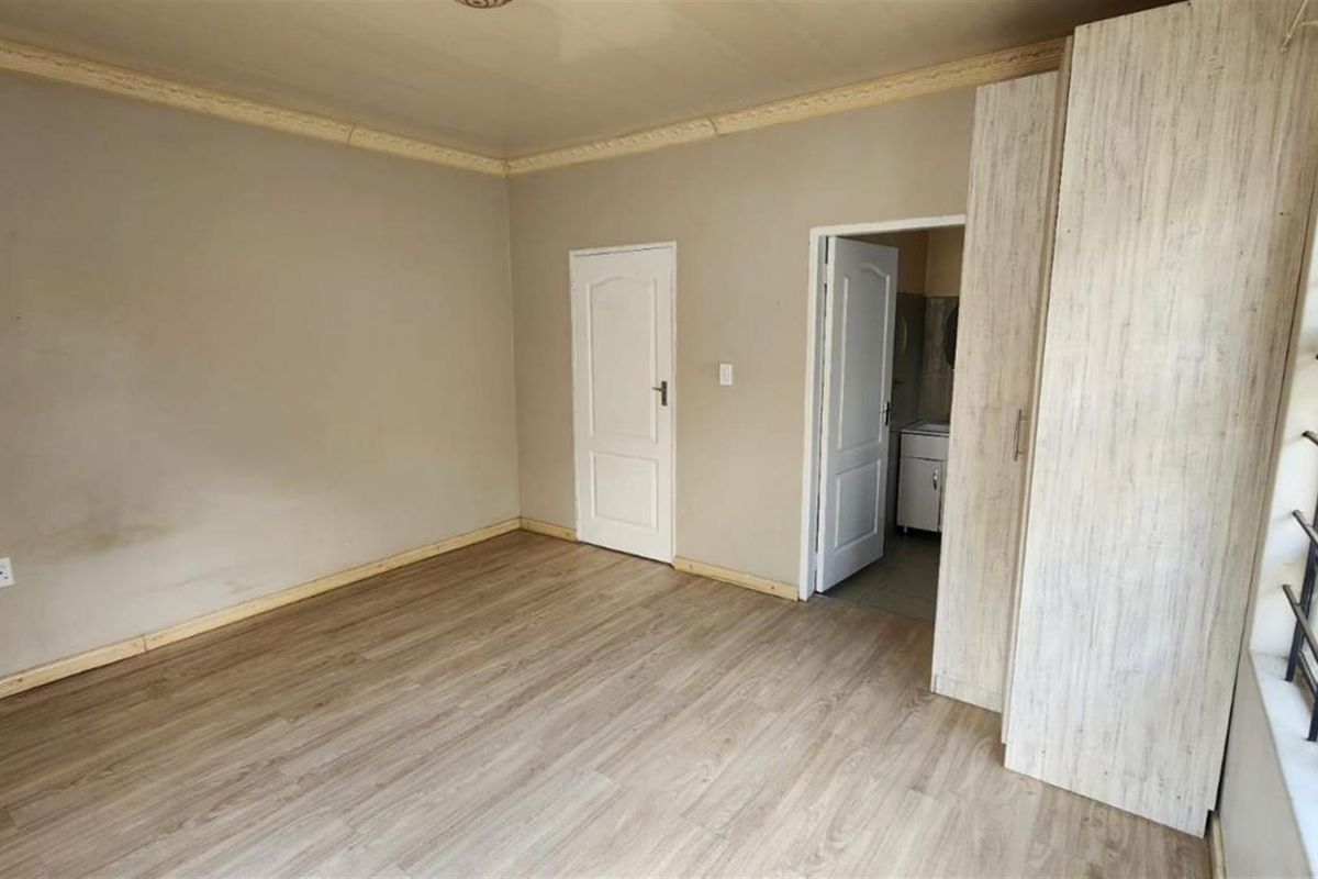 An empty bedroom featuring light wood-look laminate flooring, built-in cupboards, and security bars on the window.