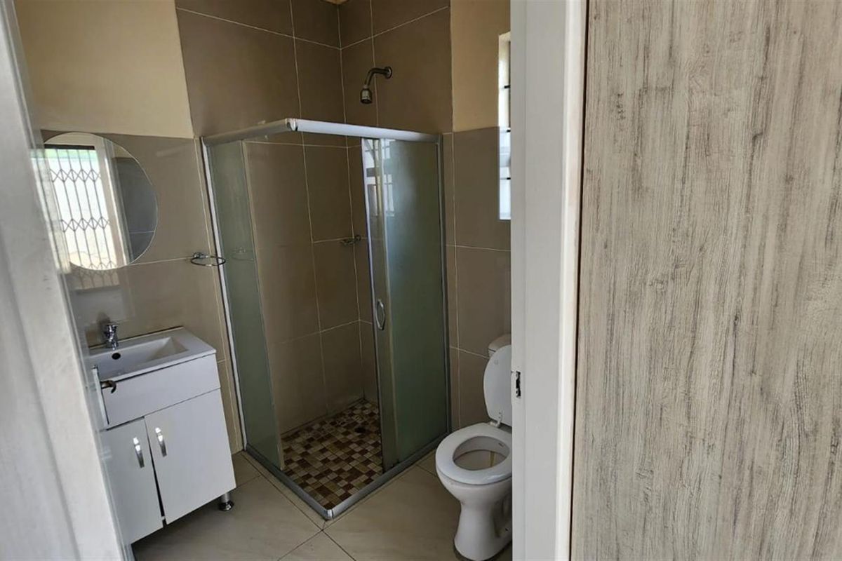 A clean, functional bathroom featuring a glass shower enclosure, a modern vanity with basin, and a standard toilet with neutral wall tiling.