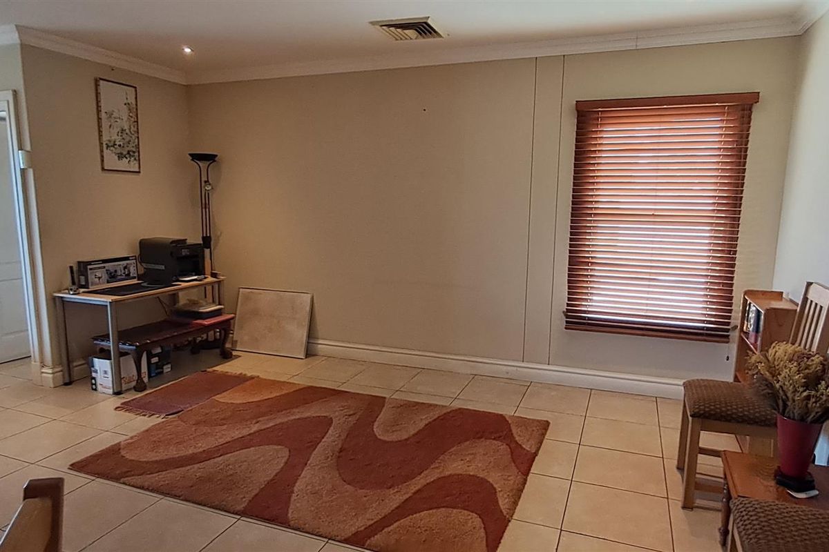 A spacious living area featuring neutral tiled flooring, recessed ceiling lighting, and wooden venetian blinds, offering a versatile layout for comfortable living.