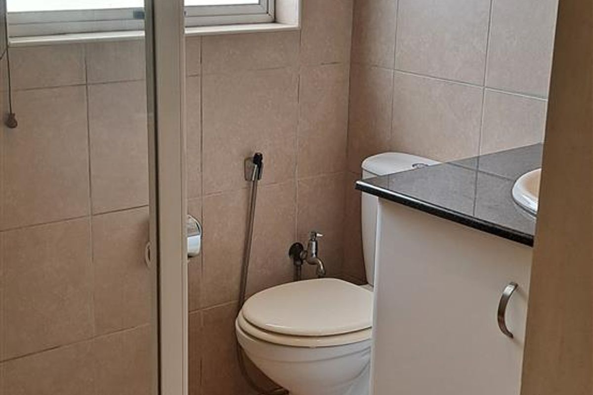 A compact bathroom featuring a glass-enclosed shower, a vanity with a dark countertop, and neutral wall and floor tiling.