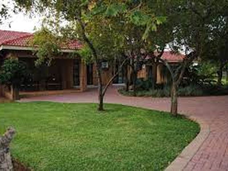 A view of the farm property featuring a paved driveway, manicured lawn, mature trees, and a covered patio area leading to the main entrance.