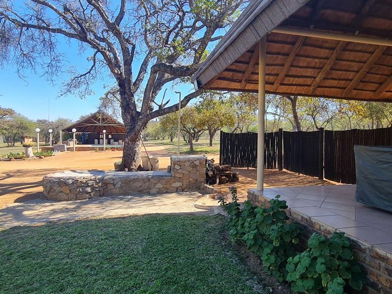 A view of the farm property featuring a covered patio with a thatched roof, stone masonry, and expansive outdoor grounds with mature trees.