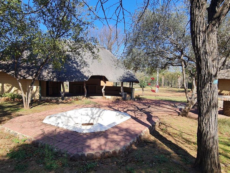 Outdoor entertainment area featuring a built-in fire pit, brick paving, and a traditional thatched-roof structure set within a natural farm landscape.