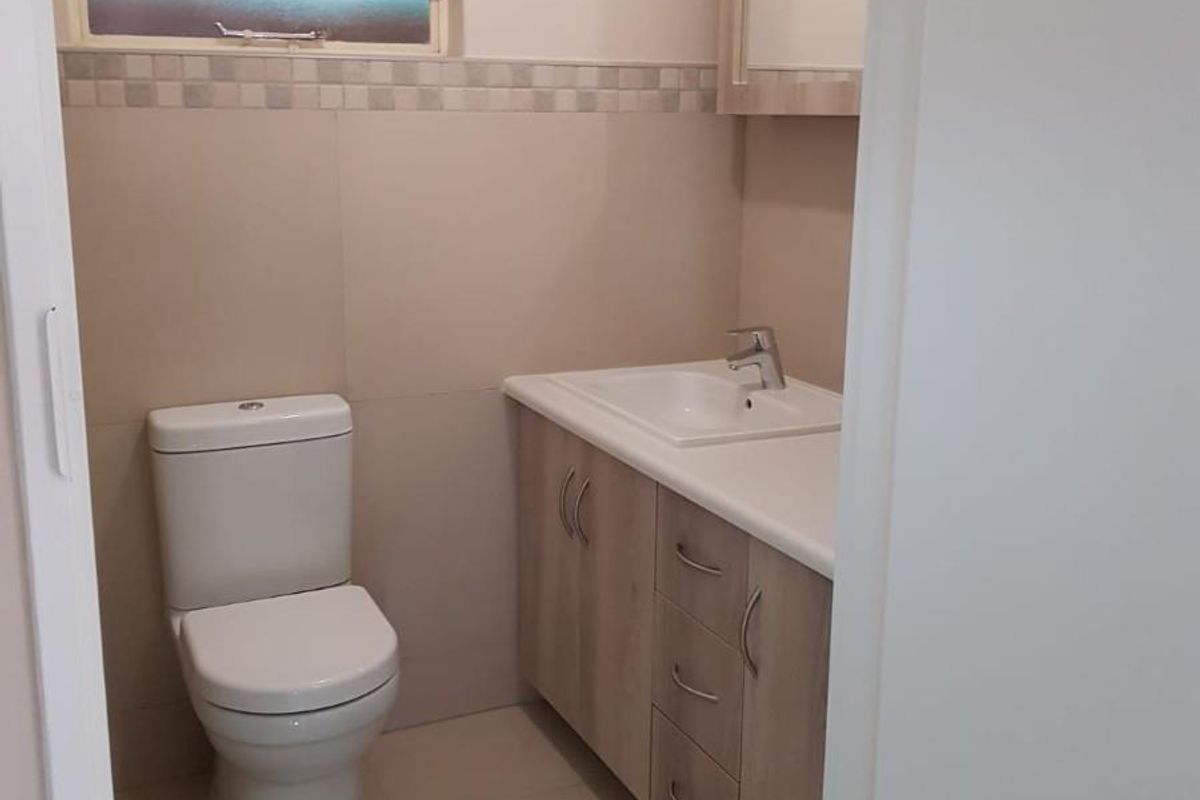 A clean and functional bathroom featuring a modern vanity with integrated basin, a toilet, and a tiled finish.