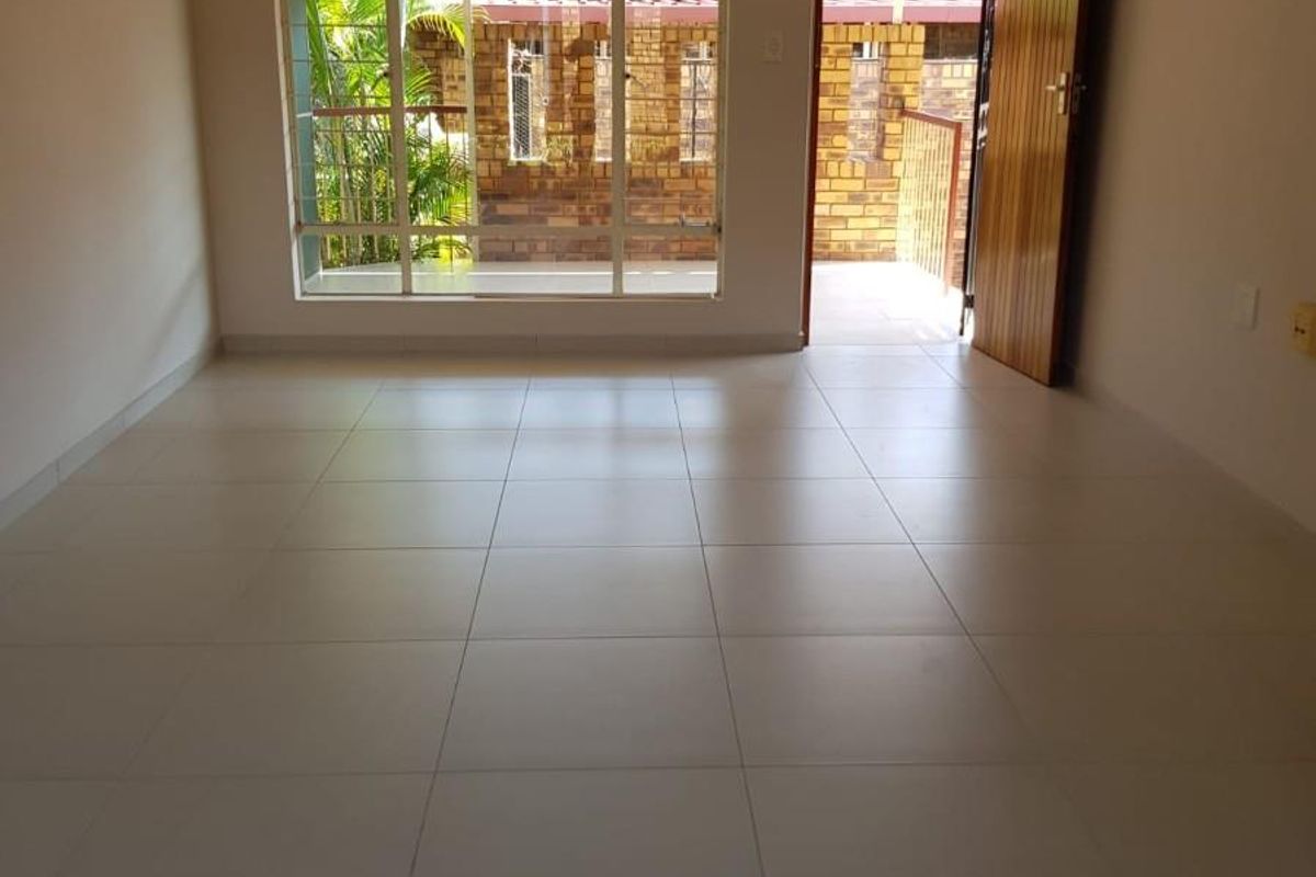 A bright, empty living room featuring neutral floor tiles, a ceiling fan, and direct access to an outdoor patio area.