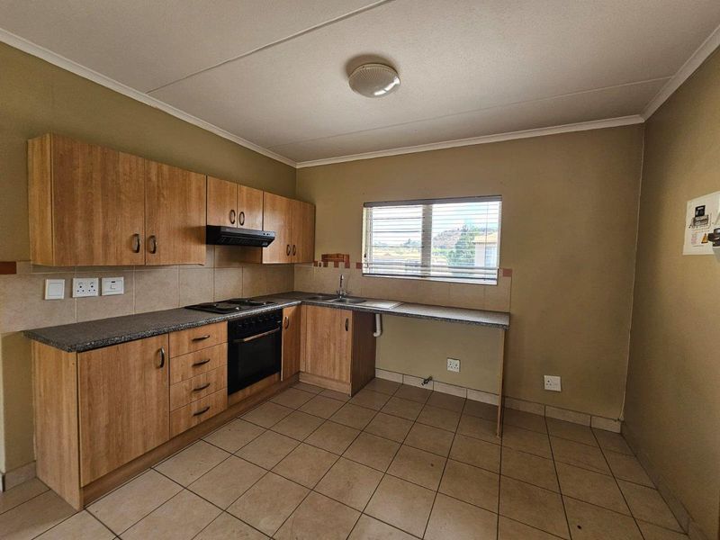 A functional kitchen featuring laminate cabinetry, built-in oven with hob, extractor fan, and tiled flooring. The space is clean and ready for updates.