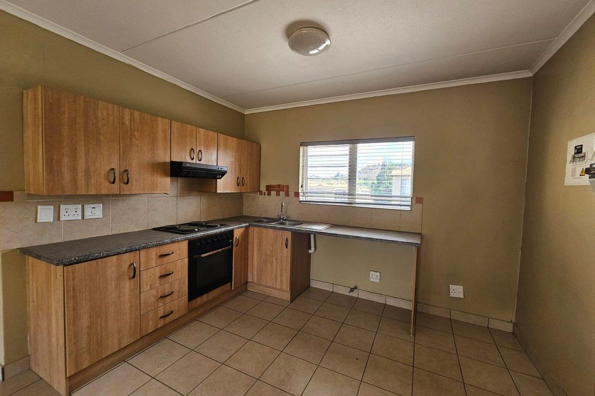 A functional kitchen featuring laminate cabinetry, built-in oven with hob, extractor fan, and tiled flooring. The space is clean and ready for updates.