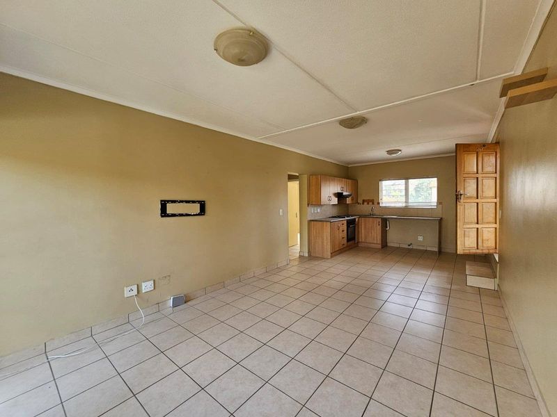 Open plan living and kitchen area featuring tiled flooring, built-in wooden cabinetry, and integrated kitchen appliances in a functional, vacant space.
