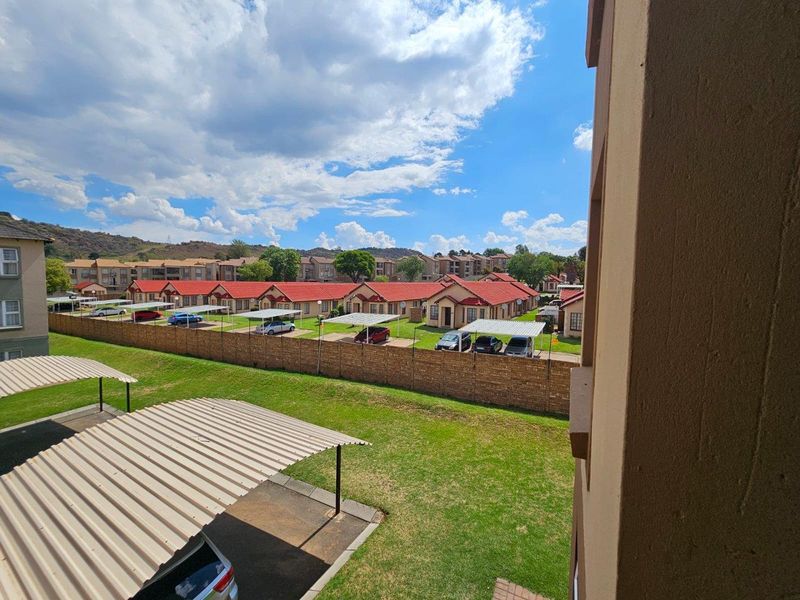 Elevated view overlooking a residential townhouse complex with carports, landscaped lawns, and brick boundary walls under a clear sky.
