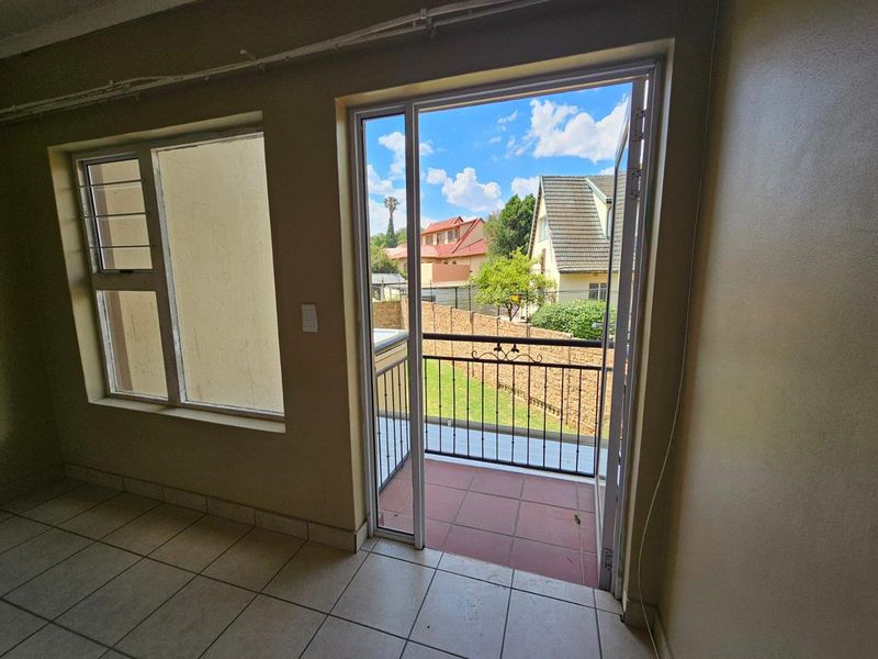 A small balcony area with tiled flooring and wrought iron railing, accessible through a glass door, overlooking a residential garden.