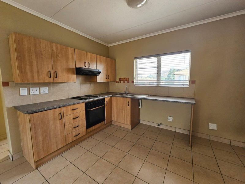 A functional kitchen featuring laminate cabinetry, built-in oven with hob, extractor fan, and tiled flooring, offering a clean and practical workspace.