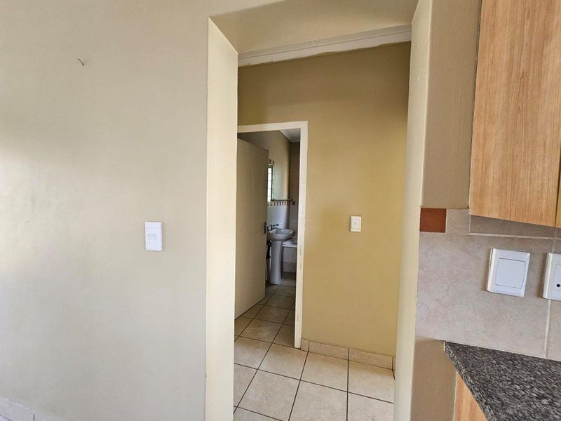 A view through a hallway connecting the kitchen area to a bathroom featuring a pedestal basin and tiled flooring.