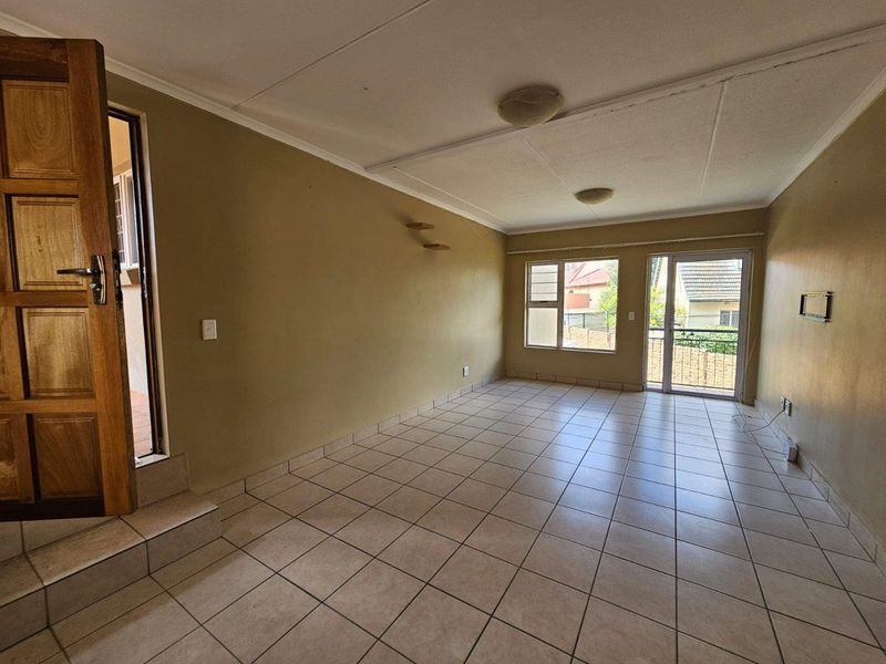 An empty, open-plan living area featuring tiled flooring, large windows, and a sliding glass door leading to the exterior.