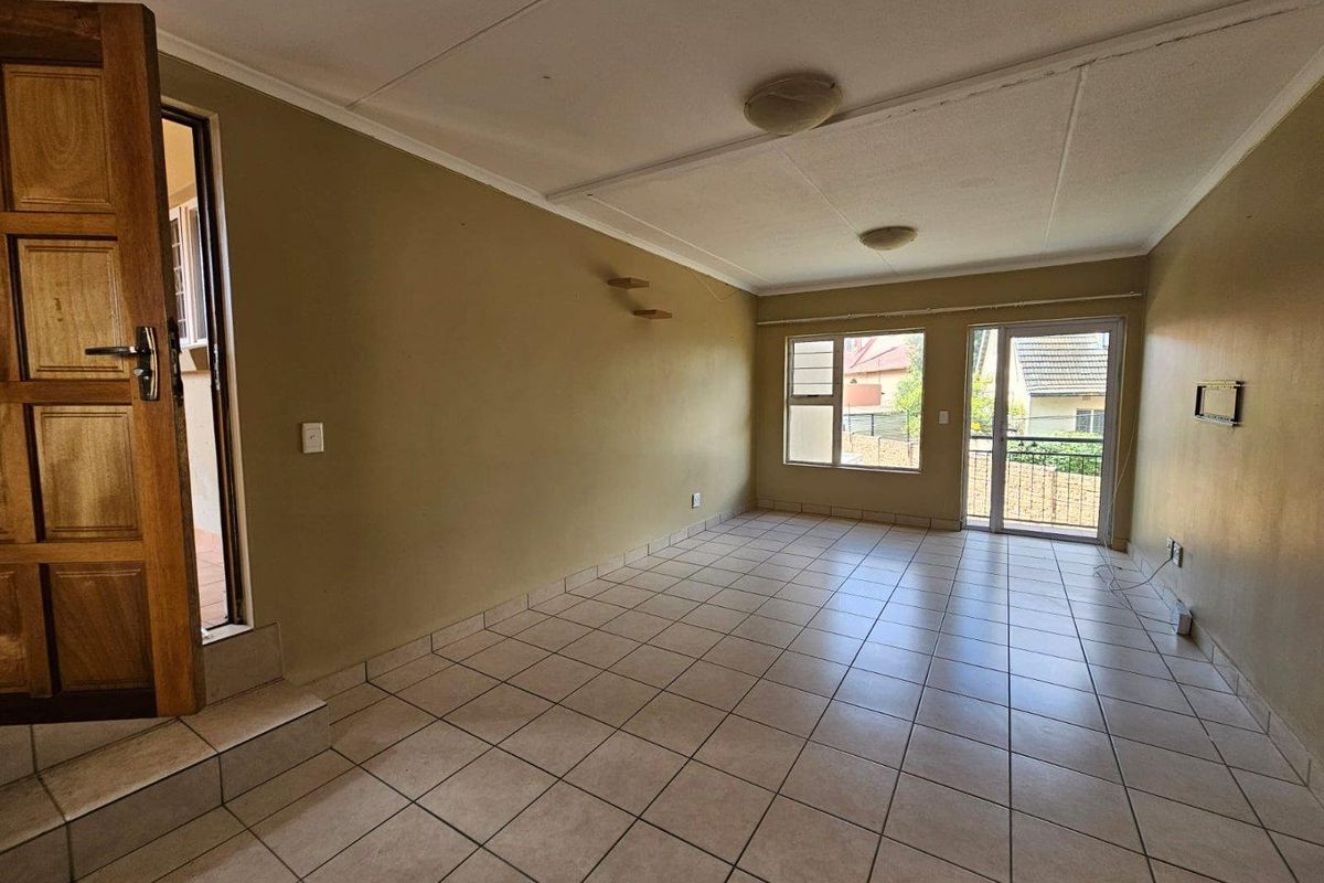 An empty, open-plan living area featuring tiled flooring, large windows, and a sliding glass door leading to the exterior.
