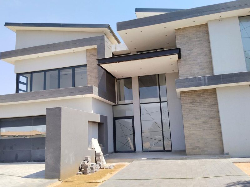 Modern double-storey residence featuring a contemporary flat roof design, large glass windows, stone cladding accents, and an integrated garage with a paved driveway.