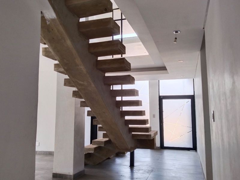 Modern entrance hall featuring a striking concrete floating staircase, tiled flooring, and a contemporary frosted glass front door.