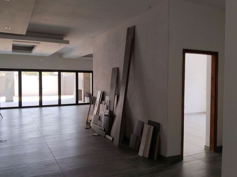 Spacious open-plan living area featuring large aluminium stacking doors, recessed ceiling details, and modern floor tiles, currently in an unfinished state.