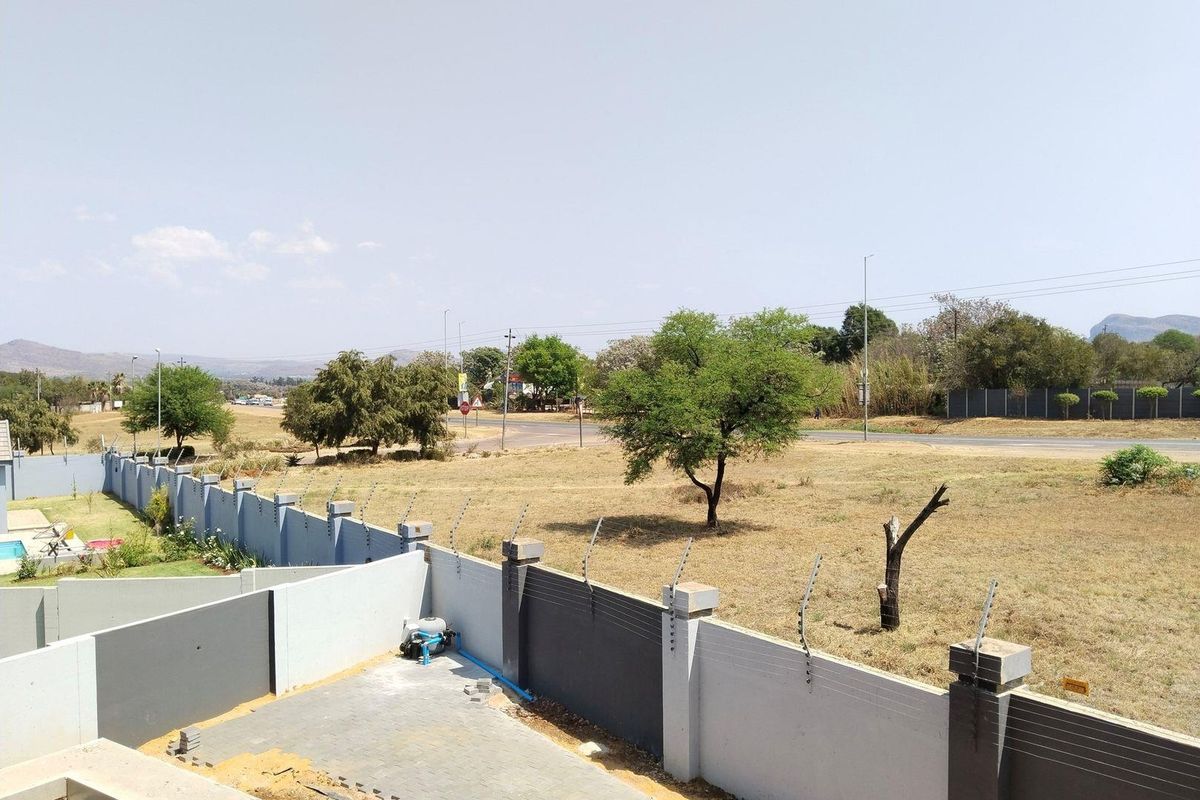 An elevated view of the rear property boundary featuring a modern perimeter wall with integrated electric fencing and a paved driveway area.