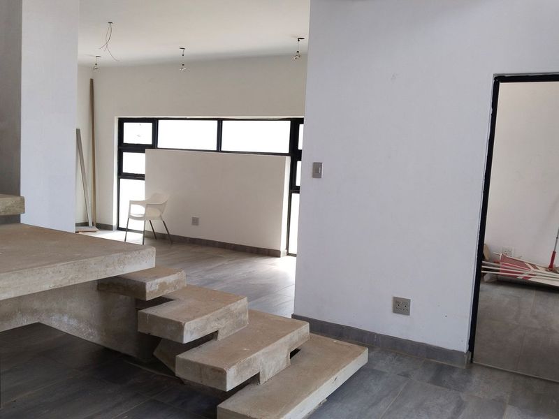 An open-plan living area featuring a modern concrete staircase, tiled flooring, and large black-framed windows, currently in an unfinished state.