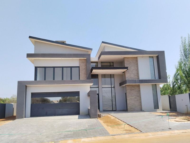 Modern double-story residential property featuring a contemporary facade, large glass windows, stone cladding, and a paved driveway with an integrated double garage.