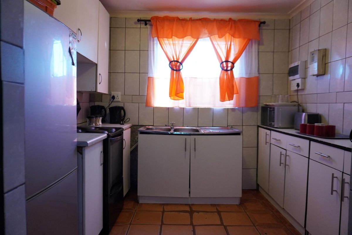 A functional kitchen featuring white cabinetry, a double-basin sink, and tiled flooring, offering a practical layout for daily meal preparation.