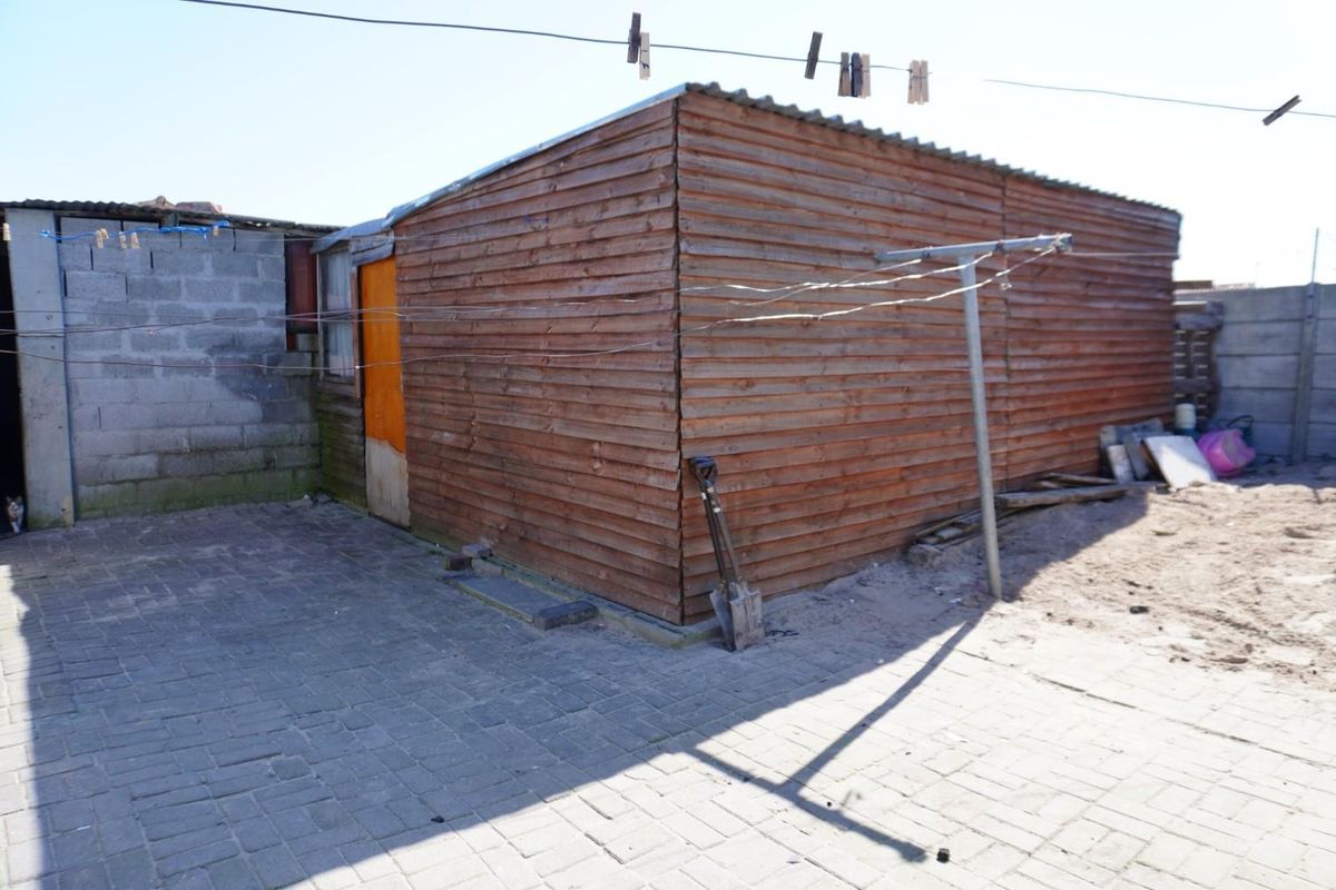 Exterior view of a timber-clad structure with a paved courtyard area and basic utility features.