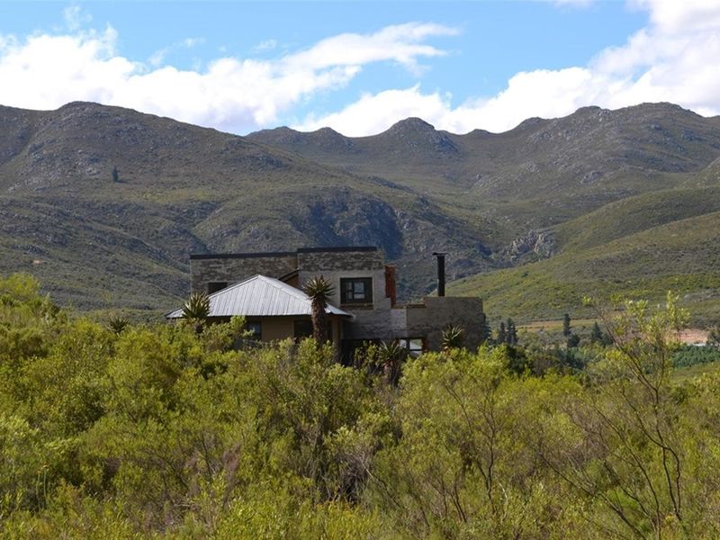 A rustic farm-style dwelling featuring stone cladding and a metal roof, set against a scenic mountain backdrop.