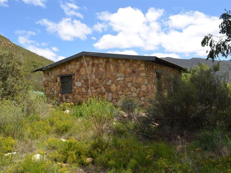 A rustic stone-clad cottage set within a natural landscape, featuring a metal roof and security-barred windows.