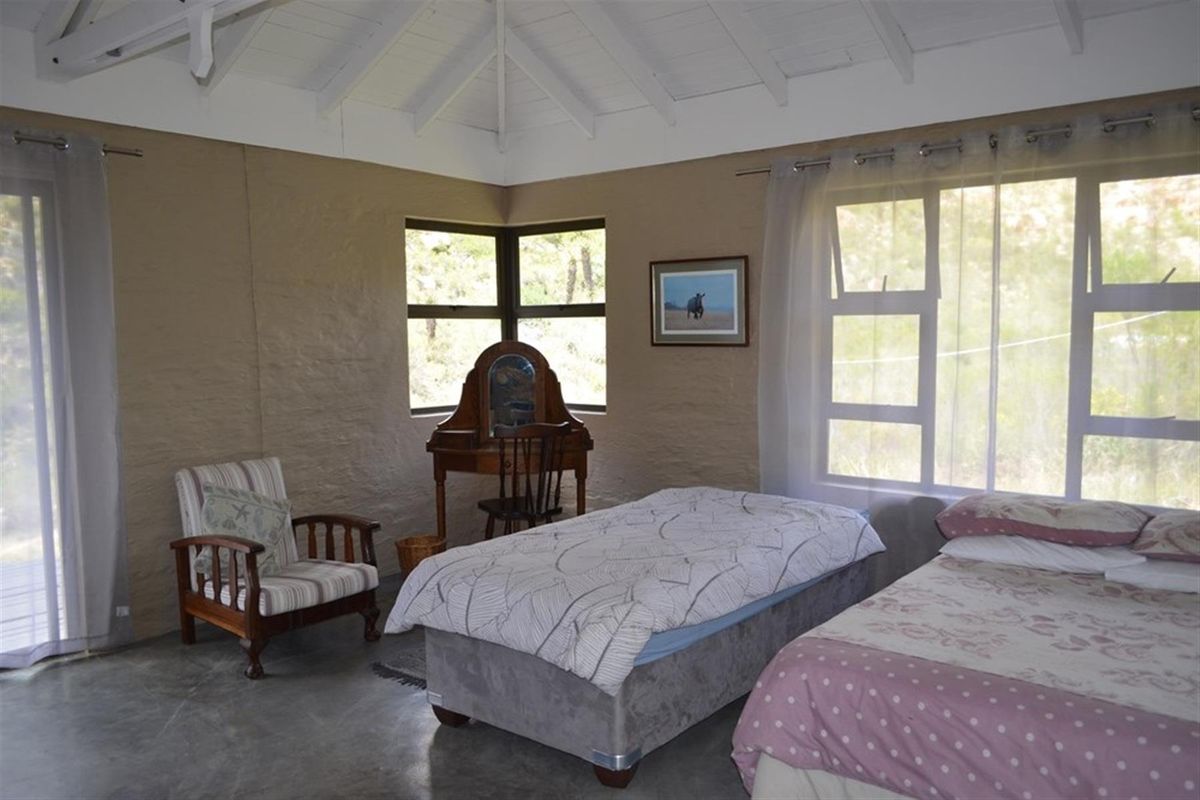 A bedroom featuring exposed timber ceiling beams, concrete flooring, and large windows providing natural light and views of the surrounding farm landscape.