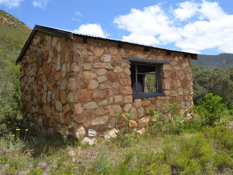 A rustic stone-walled outbuilding with a corrugated metal roof, situated in a natural landscape setting.