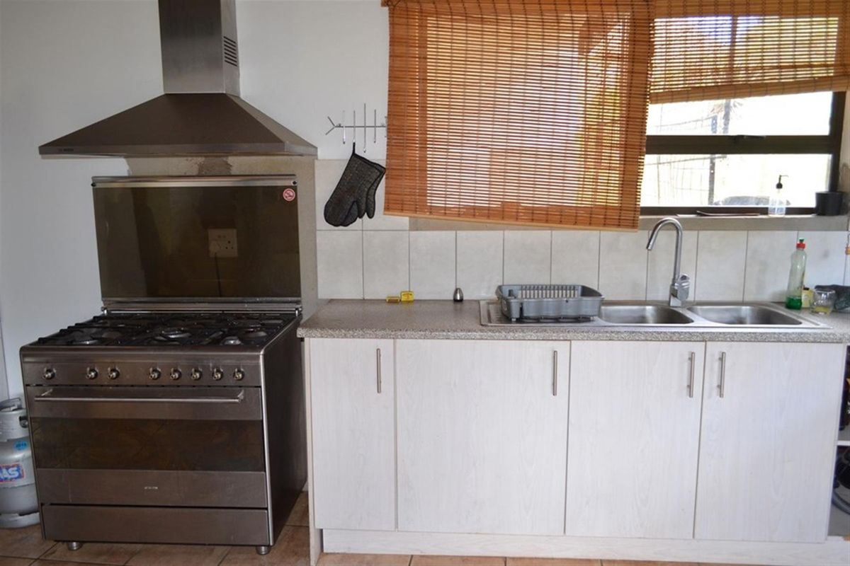 A functional kitchen area featuring a stainless steel gas stove, extractor fan, double basin sink, and laminate cabinetry with a tiled backsplash.
