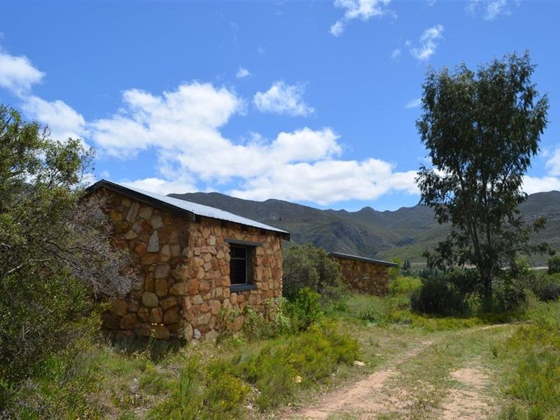 Rustic stone outbuildings situated in a rural landscape, featuring traditional masonry construction and corrugated metal roofing against a mountain backdrop.