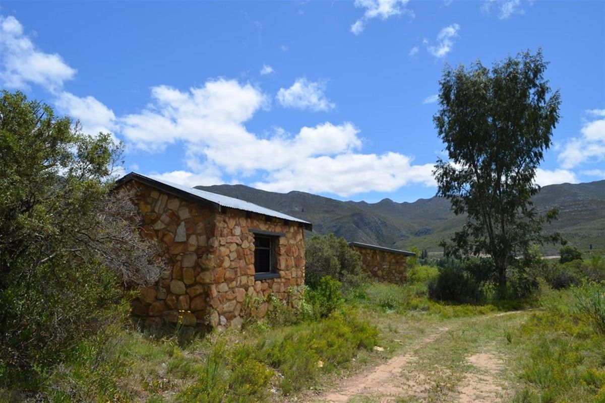 Rustic stone outbuildings situated in a rural landscape, featuring traditional masonry construction and corrugated metal roofing against a mountain backdrop.