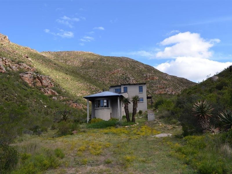 A multi-level stone farmhouse nestled in a rugged mountain landscape, featuring a covered patio and natural surroundings.