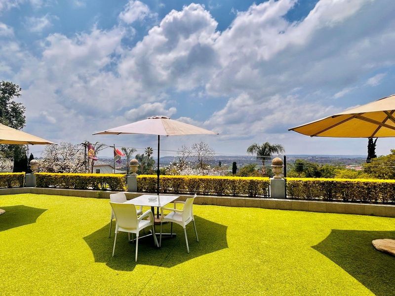 An elevated outdoor patio area featuring artificial turf, low perimeter hedging, and expansive panoramic views of the surrounding landscape.