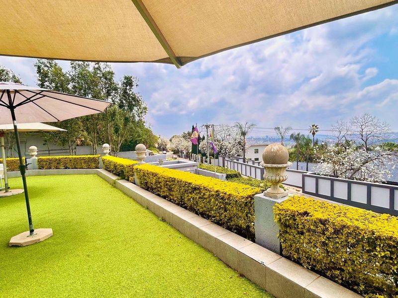 A spacious elevated patio area featuring artificial turf, stone balustrades with decorative finials, and expansive views of the surrounding landscape.
