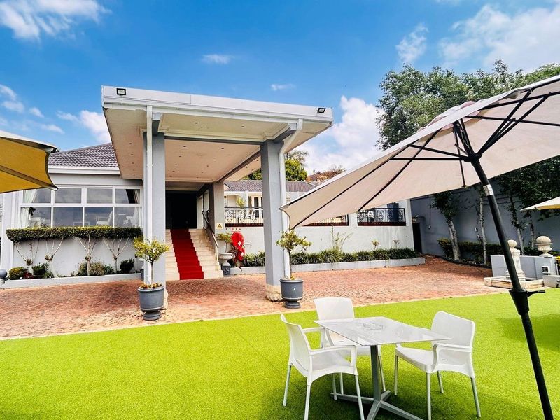 A well-maintained exterior front entrance featuring a covered portico, paved driveway, and landscaped garden area with artificial turf.