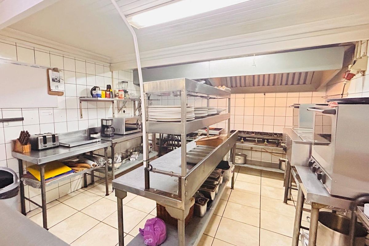A functional commercial-style kitchen featuring stainless steel work surfaces, tiled walls, and a built-in extractor hood system.