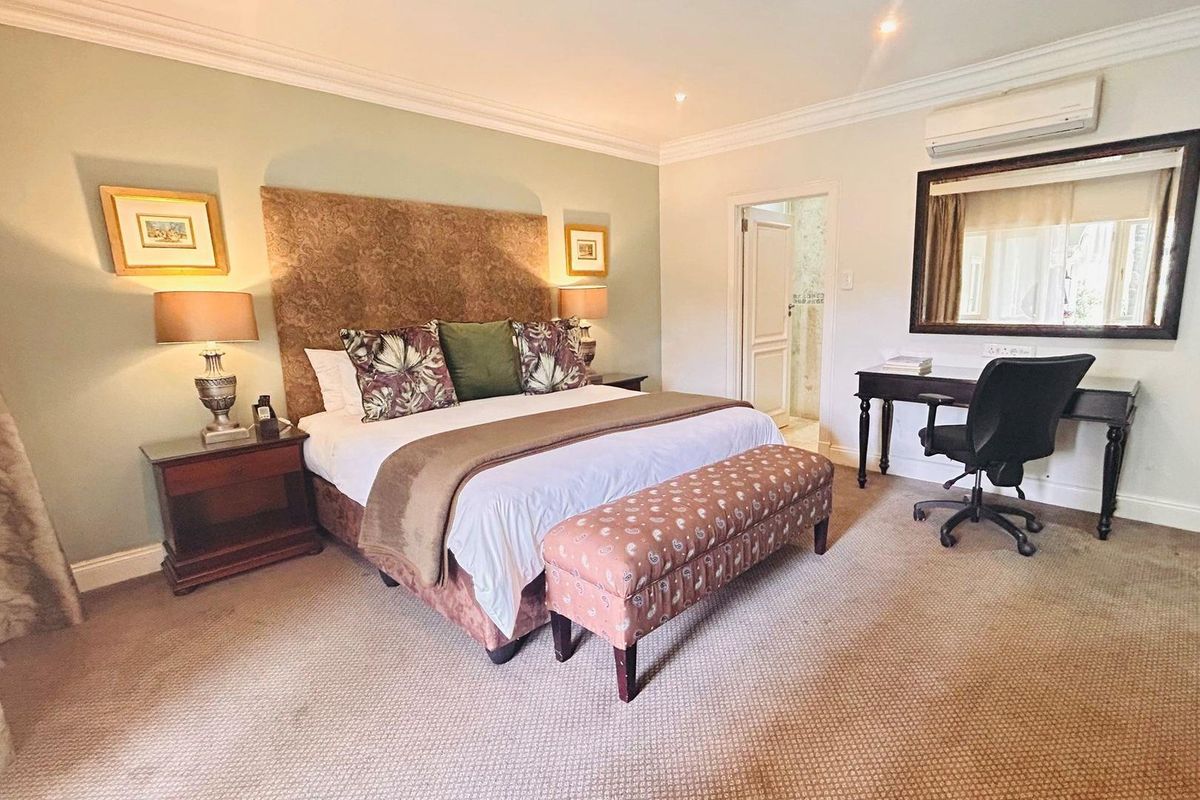 Spacious bedroom featuring crown molding, wall-to-wall carpeting, and a wall-mounted air conditioning unit, with an adjoining en-suite bathroom.